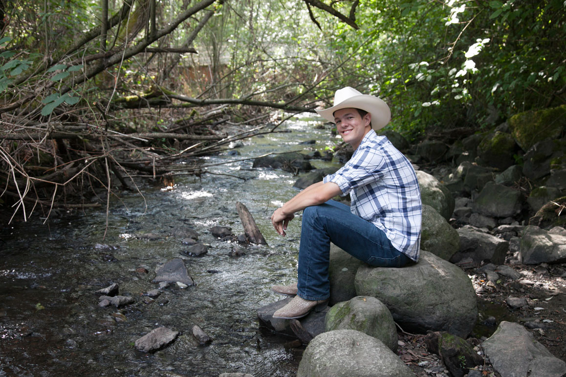 Senior boy with cowboy hat sitting along  creek at Kelsey Creek Farm