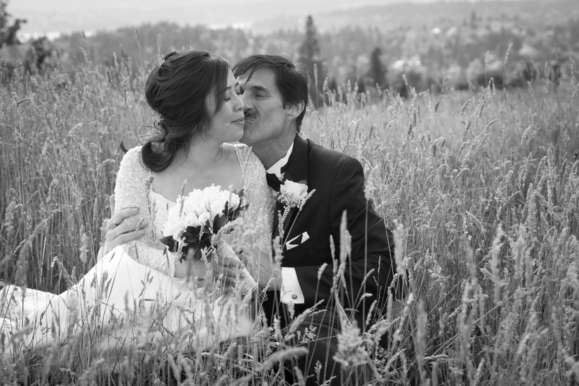 Bride and groom sitting and kissing in the tall grass at Newcastle Golf Club