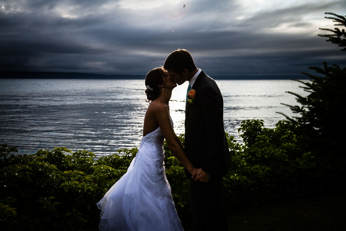 Backlit sunset photo of bride and groom kissing at Shilshole Bay Beach Club