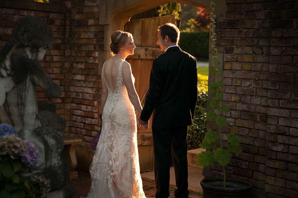 Backlit bride and groom holding hands while standing in rock archway