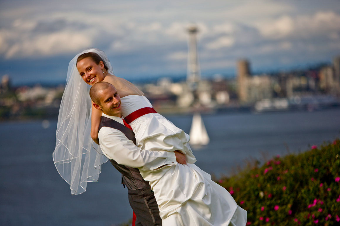 Seattle wedding photographer Tom Ellis Photography. Groom carrying bride with Seattle and Space Needle in background in West Seattle